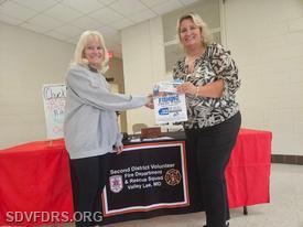 Fundraising Committee Chair DeeDee Johnson presents Michelle Trossbach with her certificate for winning the Charter Boat Fishing Trip raffle.